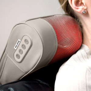 A person relaxes in a light-colored sweater and stud earrings while using the Bodi-Tek Nordic Relief Shiatsu Massager, which features visible control buttons and red heat lights, delivering deep tissue massage to their neck and upper back.