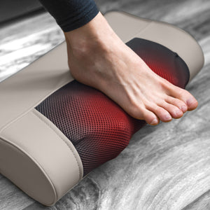 A person places their bare foot on a Bodi-Tek Nordic Relief Shiatsu Massager with beige and black design and red light, on a wooden floor.
