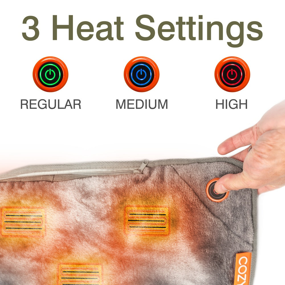 A hand presses the power button on the Cozy Wireless Rechargeable Snuggle Blanket Heated Throw. Above, three icons indicate heat settings: Regular (green), Medium (blue), and High (red), with "3 Heat Settings" at the top.