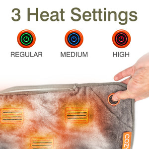 A hand presses the power button on the Cozy Wireless Rechargeable Snuggle Blanket Heated Throw. Above, three icons indicate heat settings: Regular (green), Medium (blue), and High (red), with "3 Heat Settings" at the top.