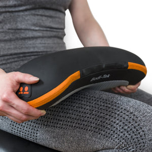 A person in gray athletic wear holds the Neck, Shoulder & Body Shiatsu Massager—black and orange with visible control buttons on the left—on their lap.