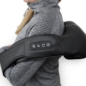 A person in a gray zip-up sweater uses the Neck & Shoulder Shiatsu Massager with side control buttons, resting it on their upper back and shoulders for deep kneading relief.