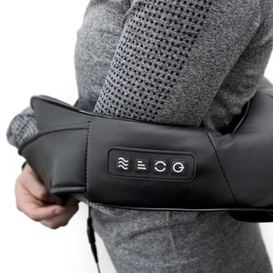 A person in a grey textured sweater uses the Neck & Shoulder Shiatsu Massager, a black device with deep kneading for shoulders and four control buttons on the side.