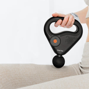 A person uses the SPORTS PERCUSSION MASSAGE GUN WITH LATERAL ACTION BELT on their thigh. The black device has a round massage head, large handle, and orange power button. It’s ideal for muscle recovery; the user wears light-colored clothing.