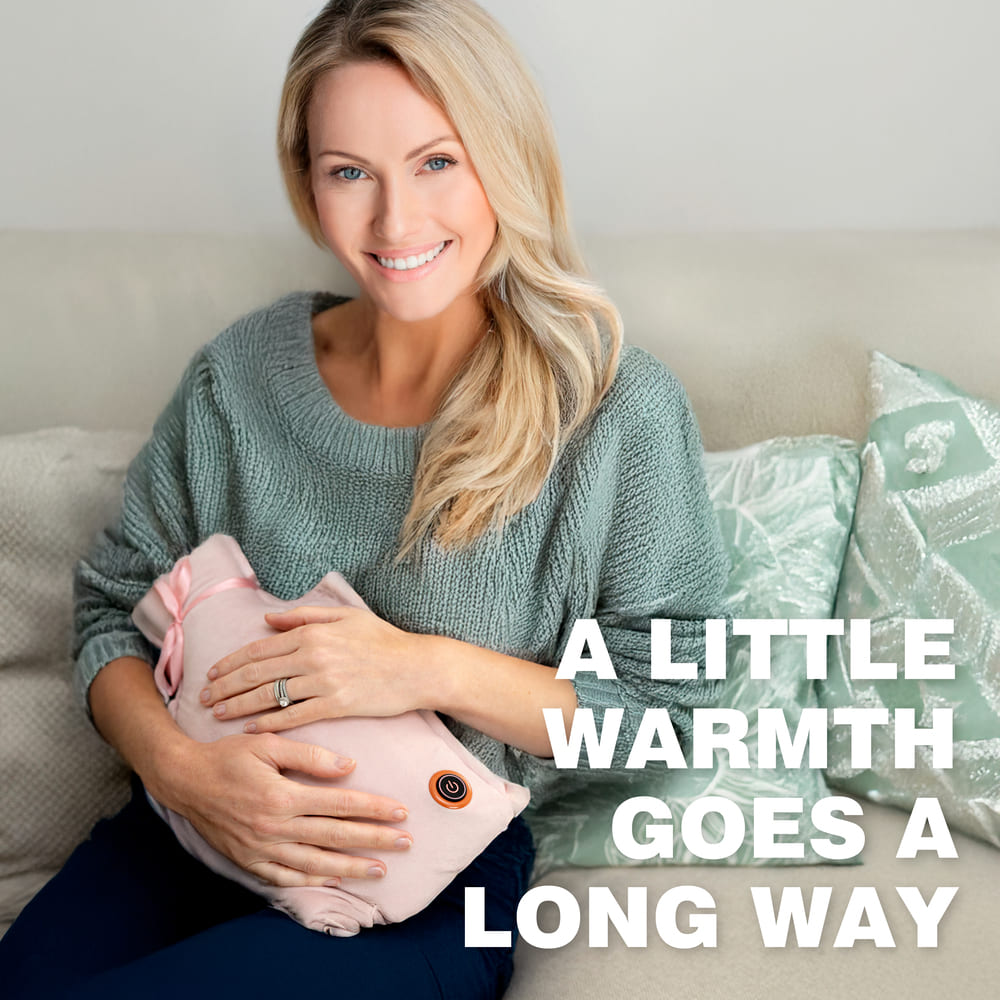 A smiling woman in a green sweater sits on a couch, holding a pink Cozy UNA Rechargeable Hot Water Bottle to her stomach. Beside her, white text reads, "A little warmth goes a long way.