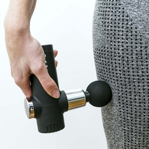 A person uses the Mini Deep Tissue Massage Gun with a round head on their thigh while wearing gray patterned athletic leggings.