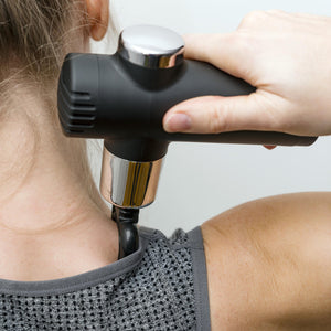 A person uses a Mini Deep Tissue Massage Gun on their neck and shoulder while wearing a sleeveless gray textured top, holding the portable massager in their right hand.