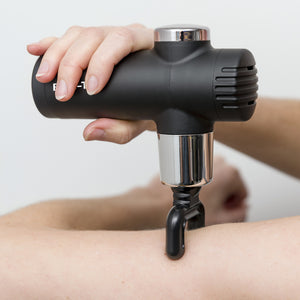 A person uses the Mini Deep Tissue Massage Gun with a fork attachment to massage their forearm against a plain white background.