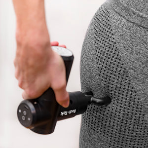 Wearing grey athletic wear, a person uses the Hot & Cold Deep Tissue Massager Gun in black on their upper thigh or hip to support muscle recovery.