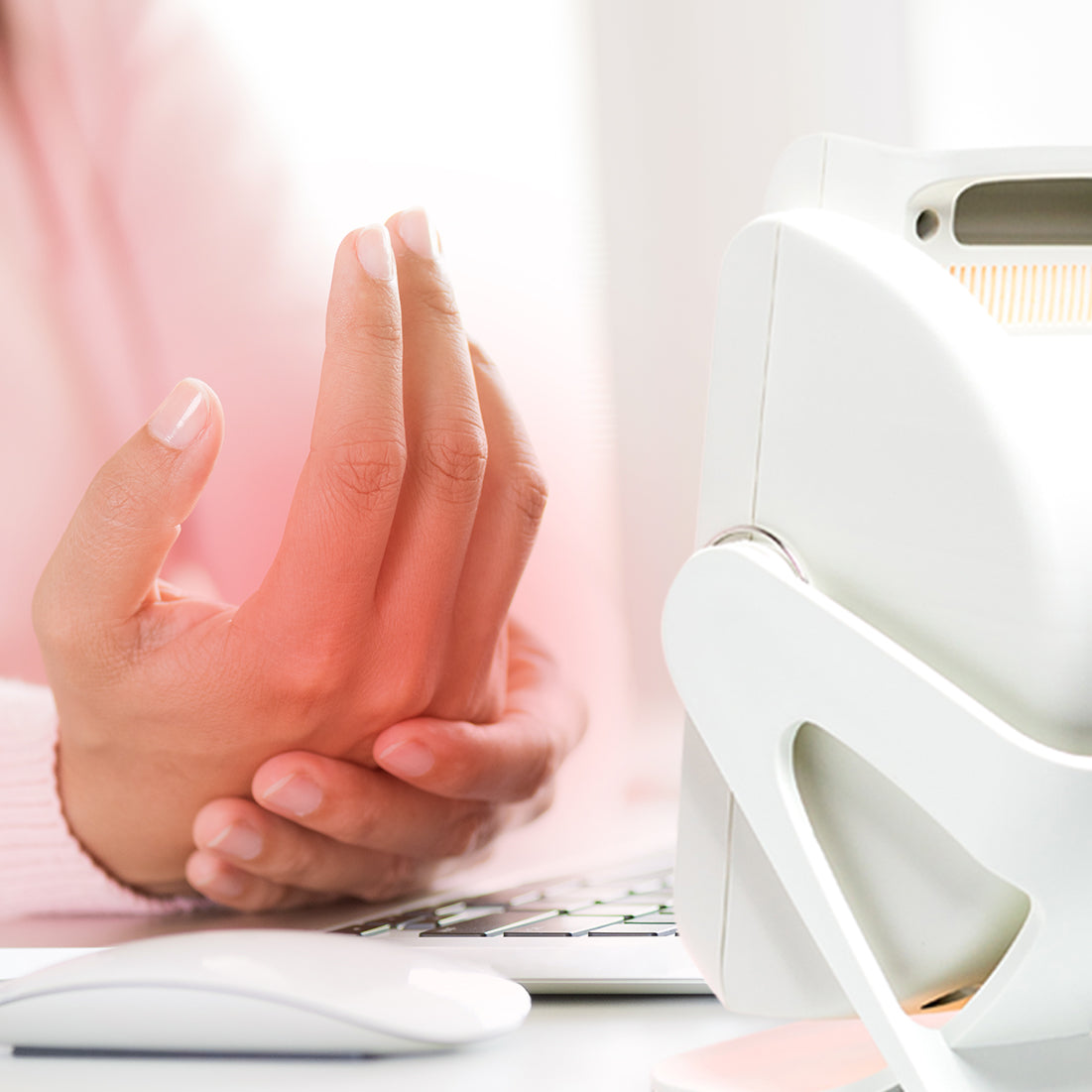 A person holds their sore wrist while using a computer, suggesting discomfort from strain—using the Infrared Heat Lamp may promote blood circulation and provide relief.