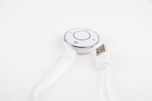 A close-up of the Circulation Plus Boost & Revive Mat, a white portable leg exerciser with a circular control panel featuring plus, minus, M, and power buttons, connected to a white USB cable on a white background.