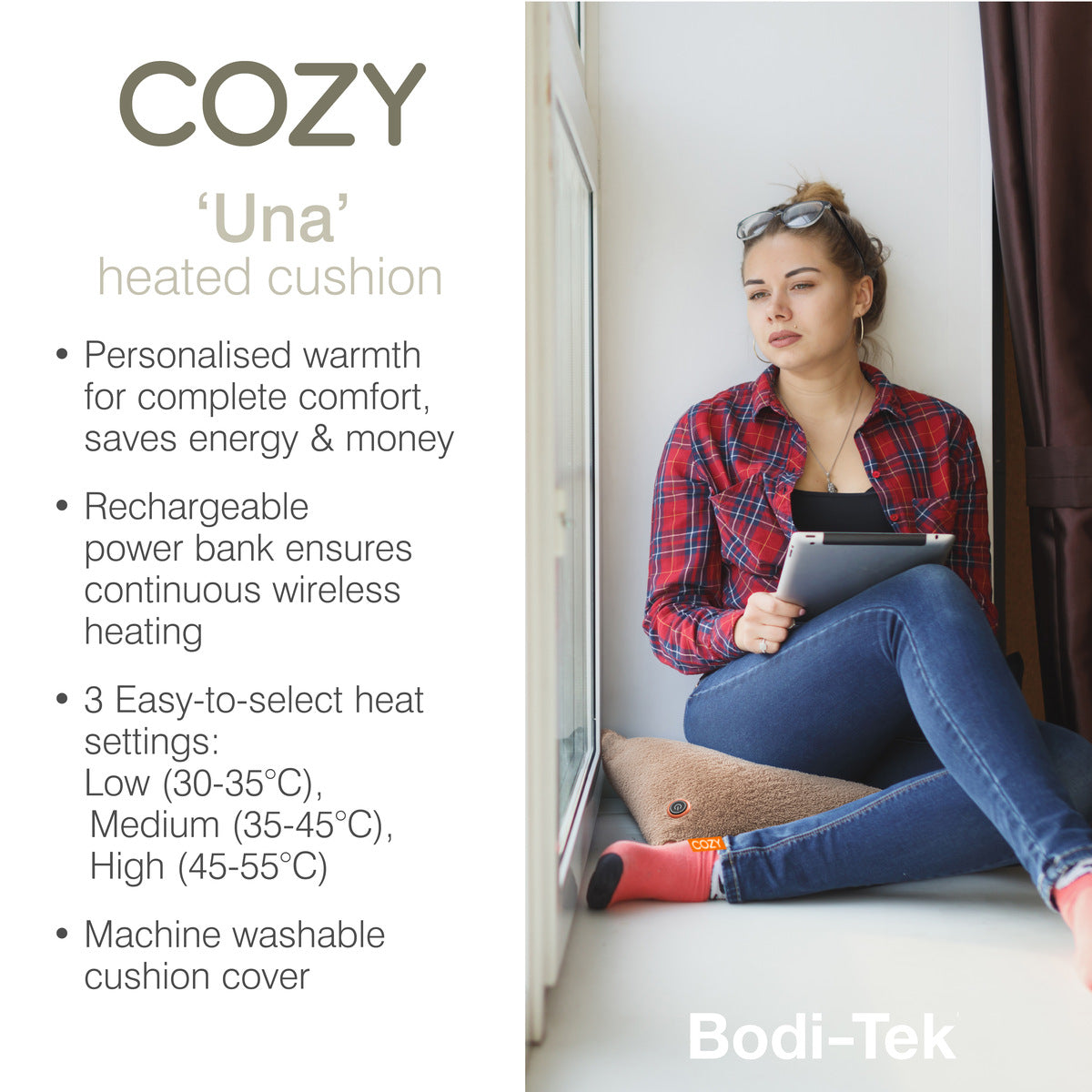 A woman in a red plaid shirt sits by a window using a tablet, her feet resting on the COZY Heated Cushion Cordless - UNA Woolly (45cm x 45cm), featuring adjustable heat settings for personalized comfort.