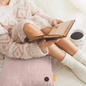 Woman reading a book leant against a pink heated cushion.