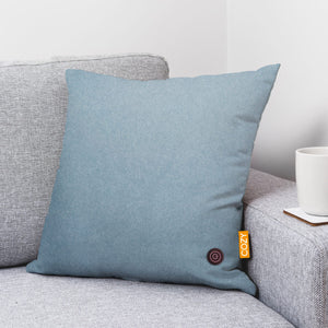 Denim Blue heated cushion shown on a grey sofa.