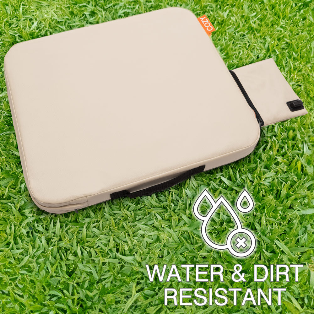 The COZY Cordless Heated Seat Pad - JORD, a beige portable seat with a handle and pull-out flap, rests on green grass. Water & Dirt Resistant icons and text appear at the bottom right.
