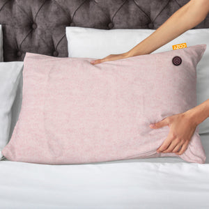 Heated pink cushion being placed amongst pillows on a bed.