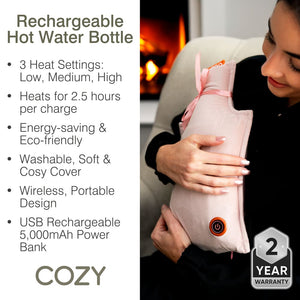 A woman holds the Cozy UNA Rechargeable Hot Water Bottle, a soft pink electric cushion with an orange power button. It offers 3 heat settings, up to 2.5 hours of wireless warmth, USB charging, a washable cover, and portable design.