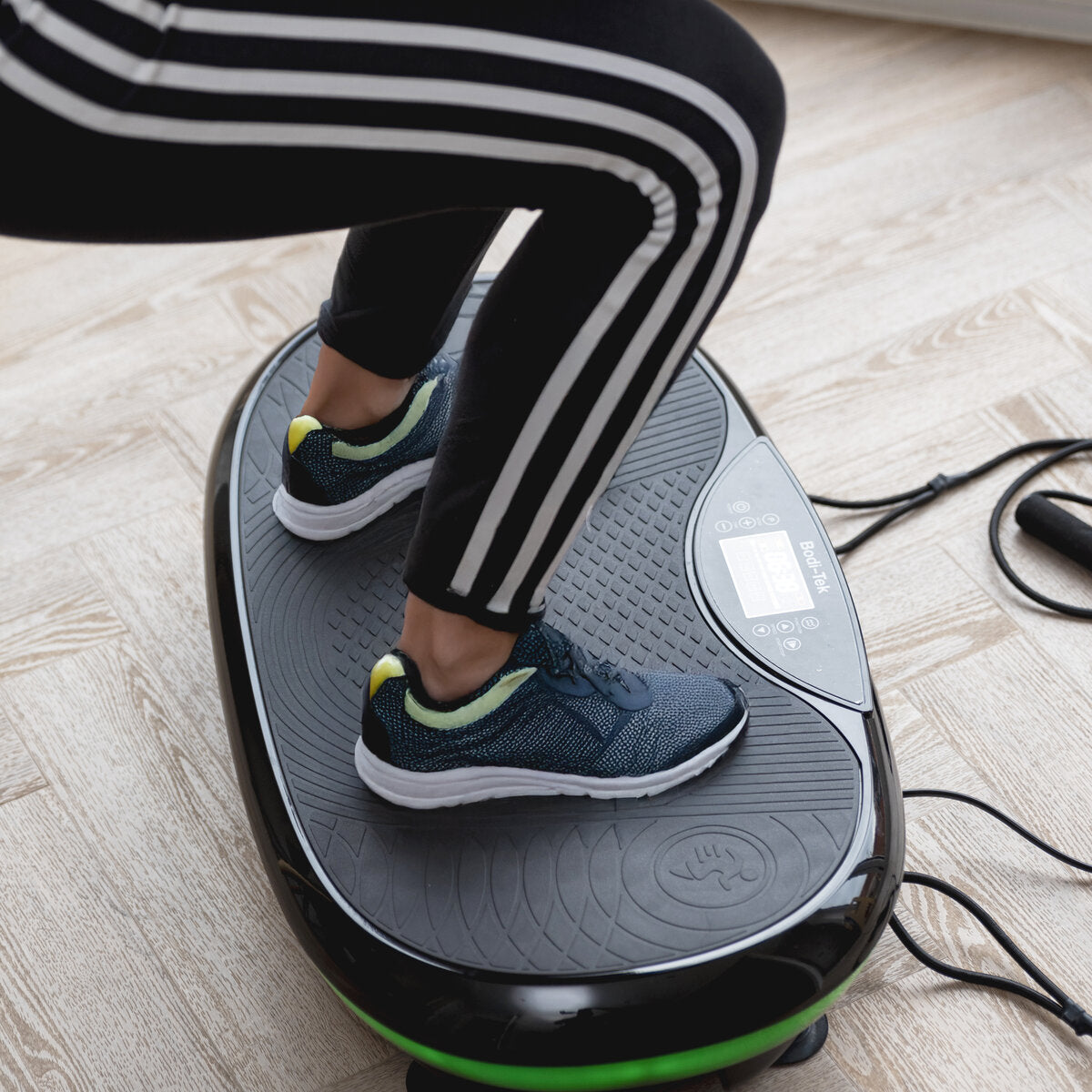 A person stands indoors on the 4D Vibration Plate Exercise Machine, featuring a digital display and control buttons; this device offers a full body workout to help burn fat.