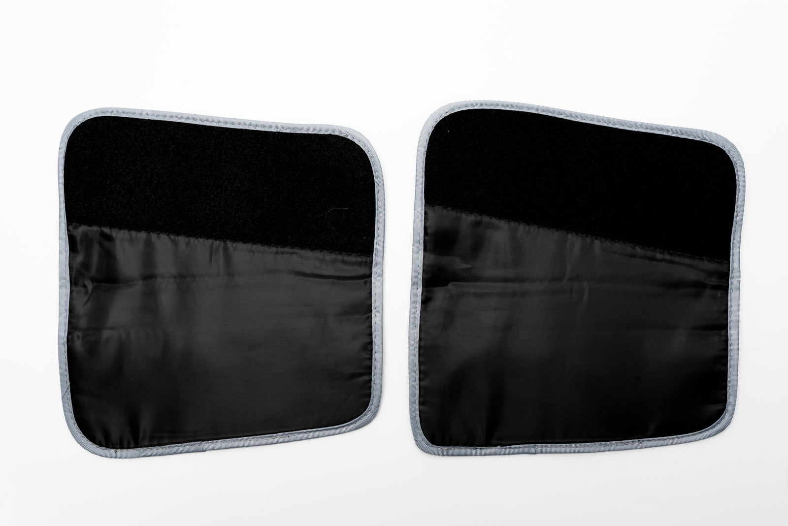 Two black rectangular fabric patches with rounded corners and gray trim, shown side by side, function as extension straps for the COMFORT360° AIR COMPRESSION MASSAGER BOOT. Each features a textured surface for secure attachment.