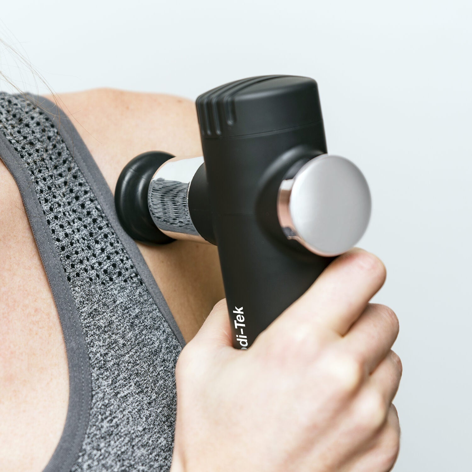A person uses the Mini Deep Tissue Massage Gun on their shoulder while wearing a gray athletic tank top.