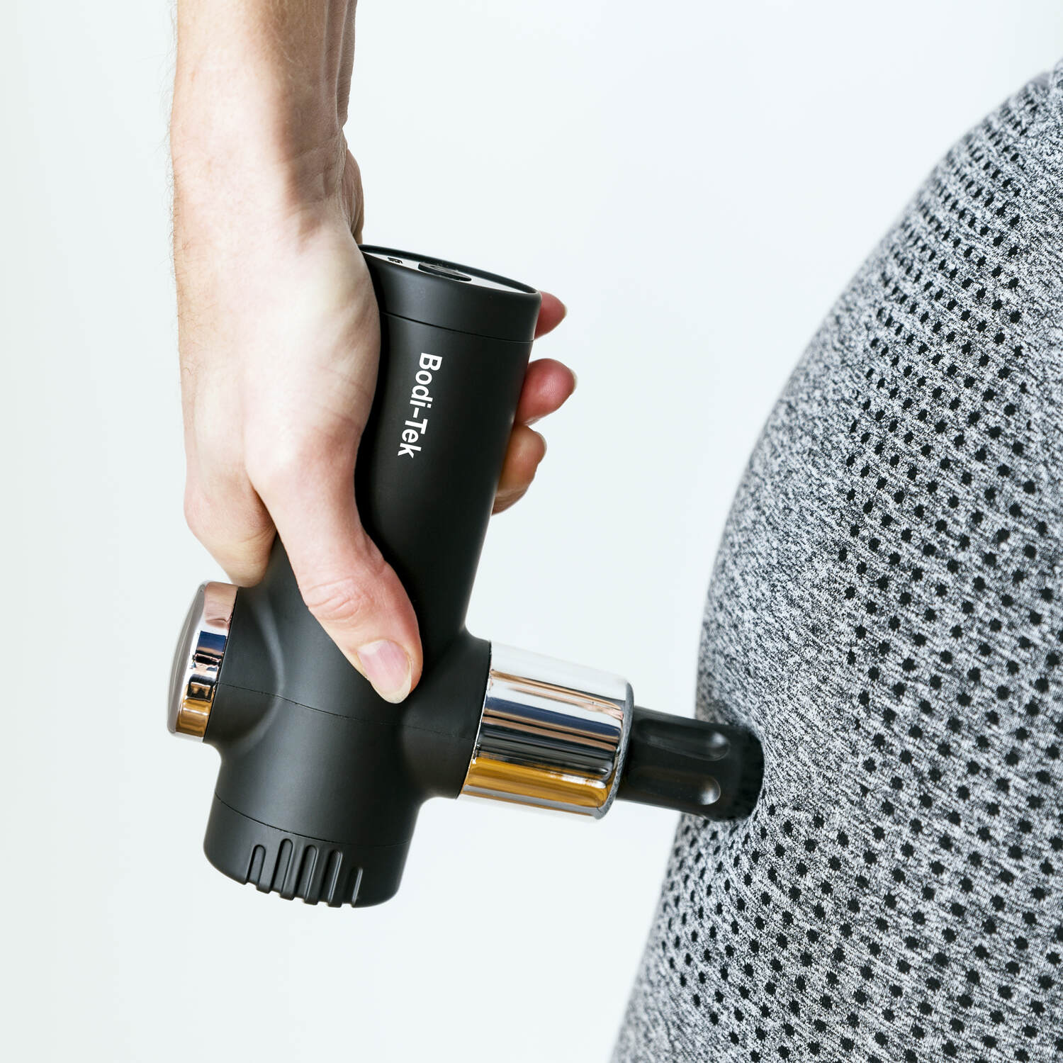 A person uses a black Mini Deep Tissue Massage Gun with a round attachment on their side, pressing it against gray, textured clothing.