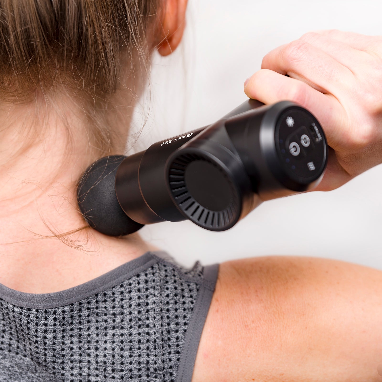 Wearing a gray textured athletic top, a person uses the Hot & Cold Deep Tissue Massager Gun, in black, on their neck and shoulder for effective muscle recovery.