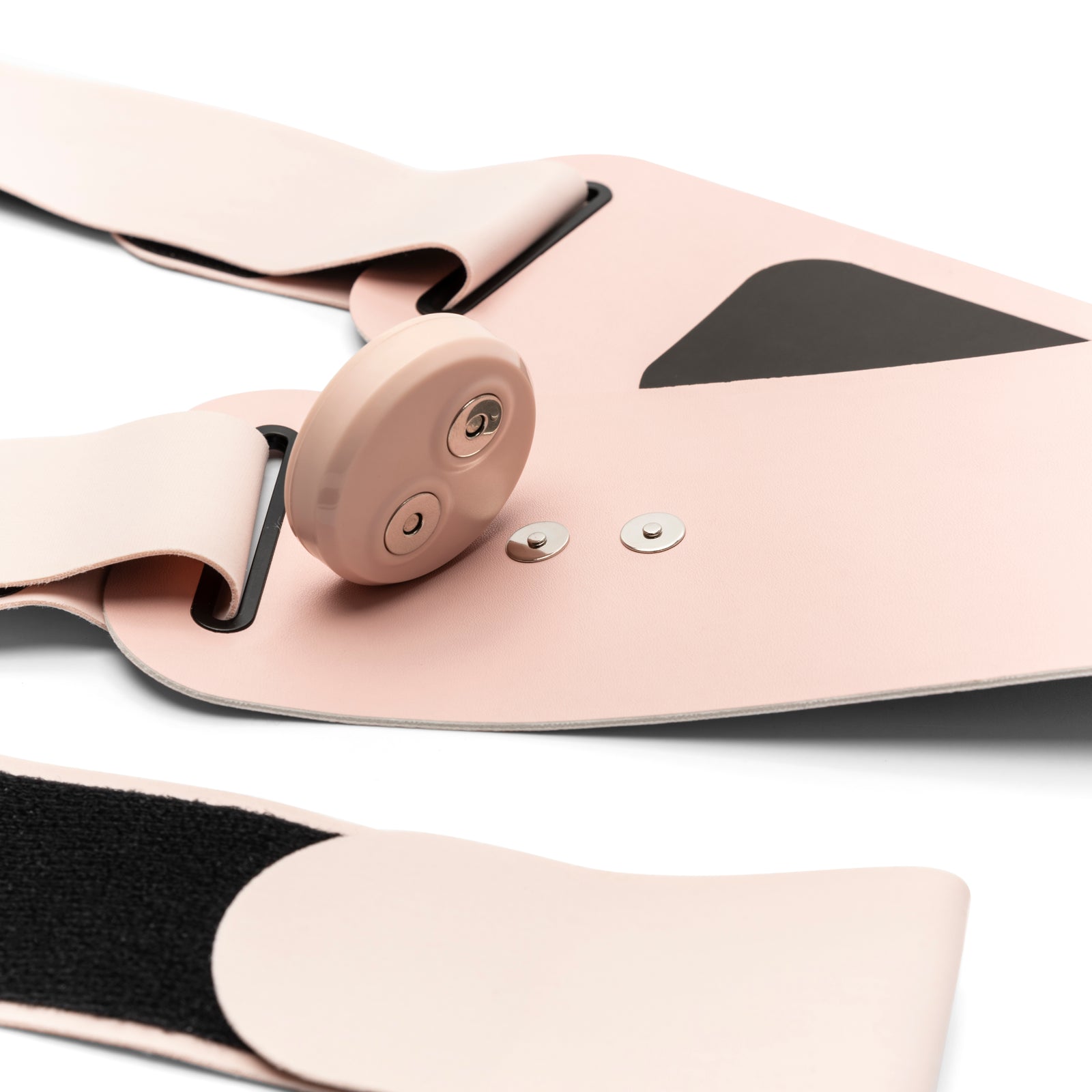 A close-up of the Ab, Tone & Shape light pink wearable electronic device with a round control button, snap fasteners, black accents, and Velcro details for muscle stimulation, displayed on a white surface.