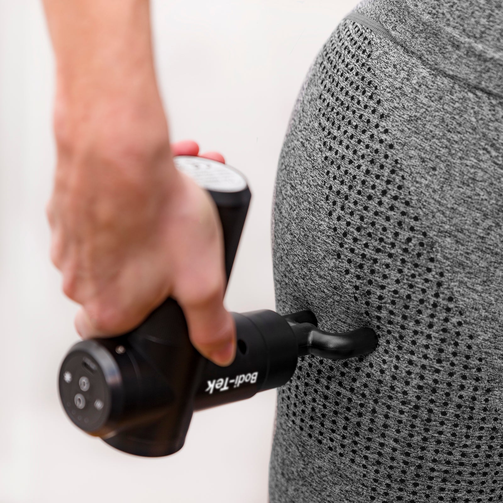 Wearing grey athletic wear, a person uses the Hot & Cold Deep Tissue Massager Gun in black on their upper thigh or hip to support muscle recovery.