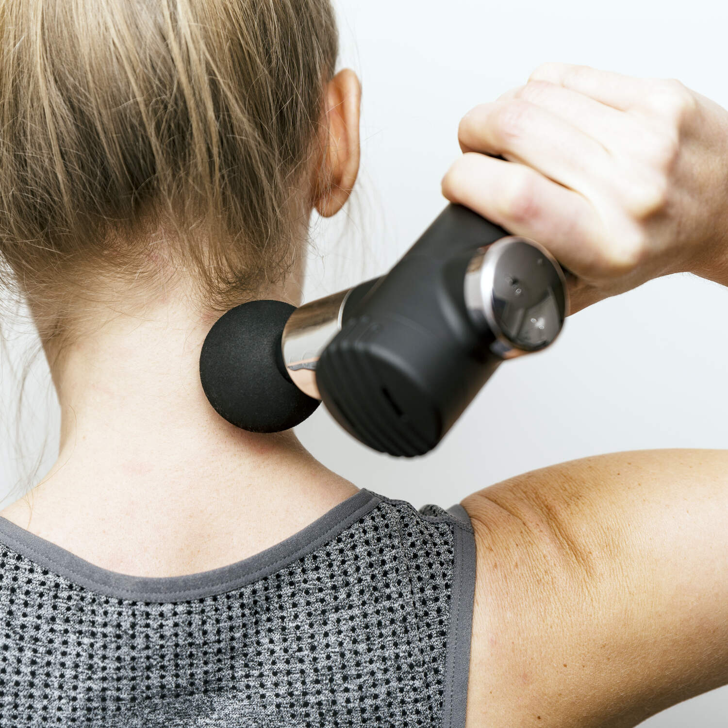 A person in a gray sleeveless top uses the Mini Deep Tissue Massage Gun on the back of their neck and upper shoulders, enjoying targeted relief with this portable, black percussive massager.