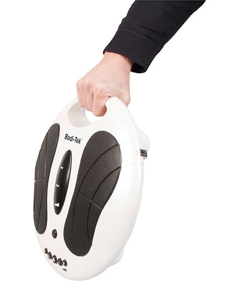 A person’s hand holds a white, oval-shaped Circulation Plus Active Lower Leg & Foot Exerciser (2025) with black grip pads and buttons on one side.